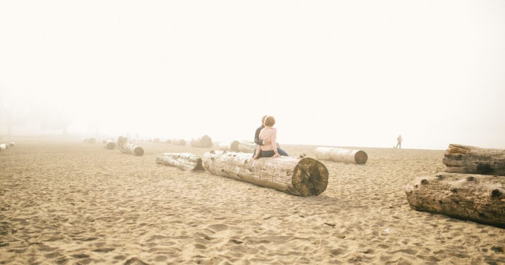 Couple sitting together on a foggy beach while healing after infidelity