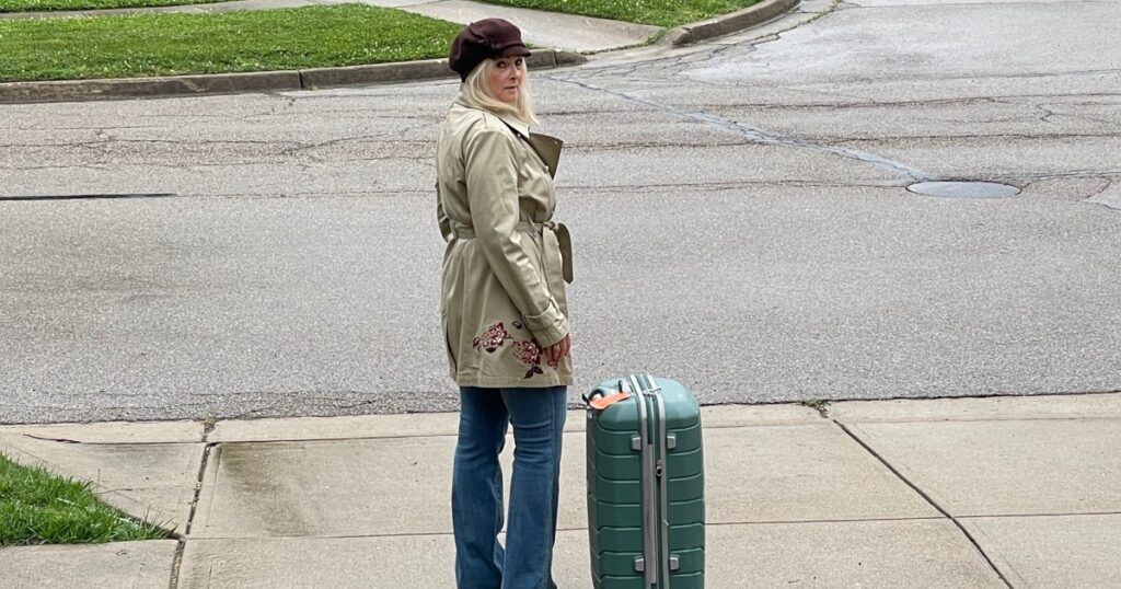 Woman standing with suitcase while deciding whether to stay or leave after infidelity